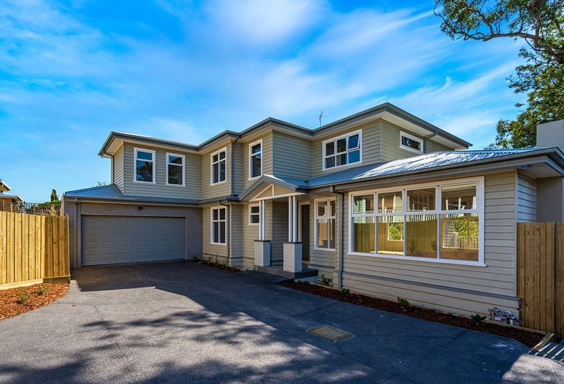 Closed metal garage door behind a green hedge and paved walkway