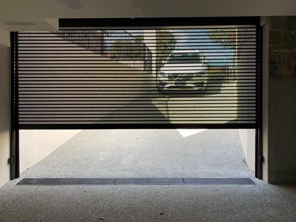 Half-open garage door with a car visible outside, sunlight streaming in