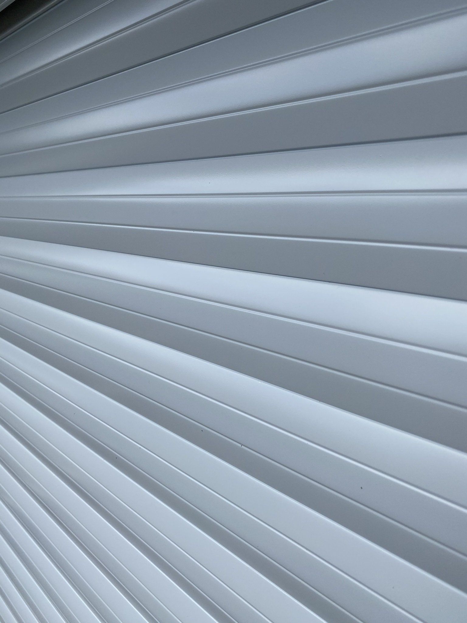 Closed white window blinds with diagonal slats and soft gray shadows