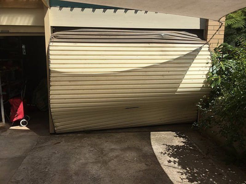 Closed beige garage door casting a shadow on a driveway beside a hedge and open doorway