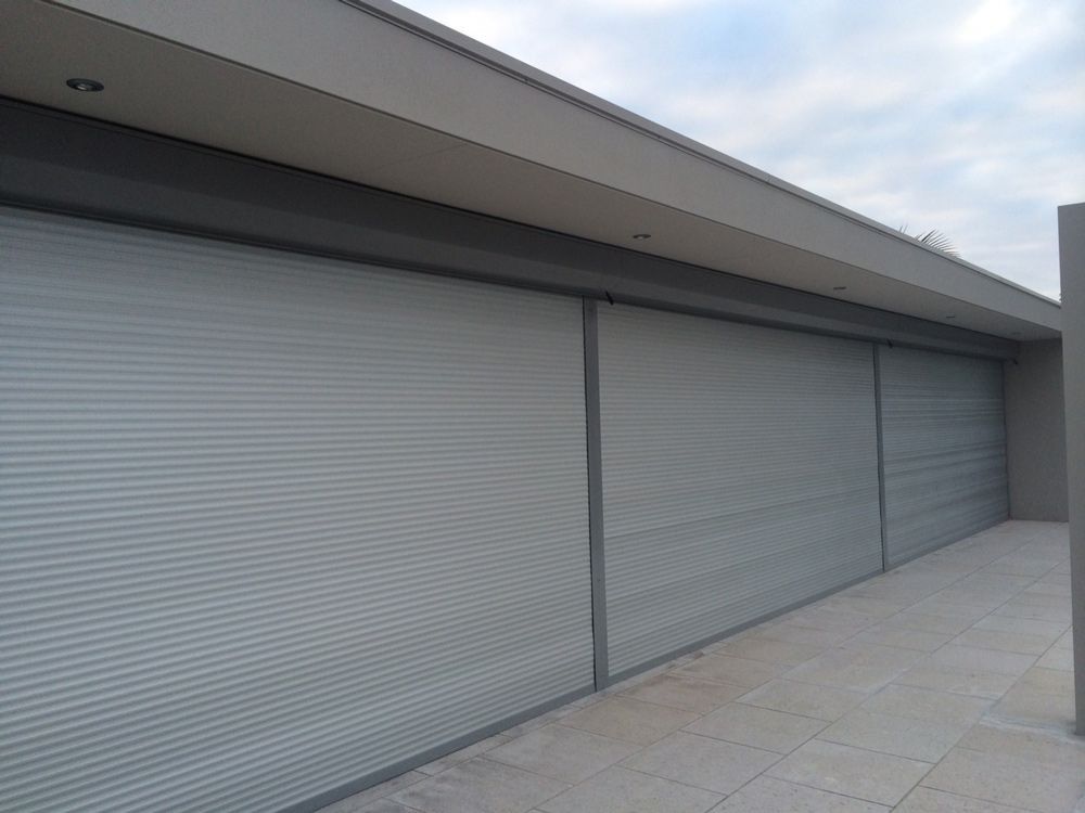Modern building exterior with large gray roller shutters and a tiled walkway