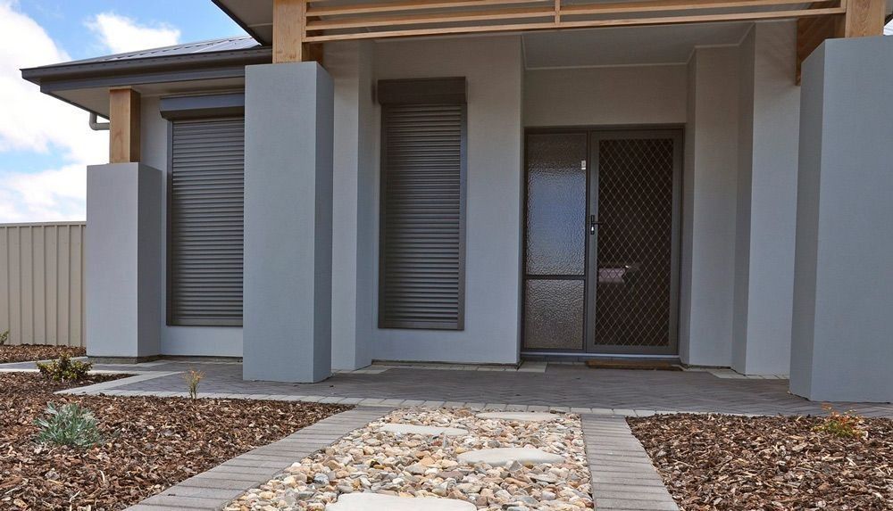 Modern house front entrance with gray walls, a doorway, and a stone pathway leading to the porch