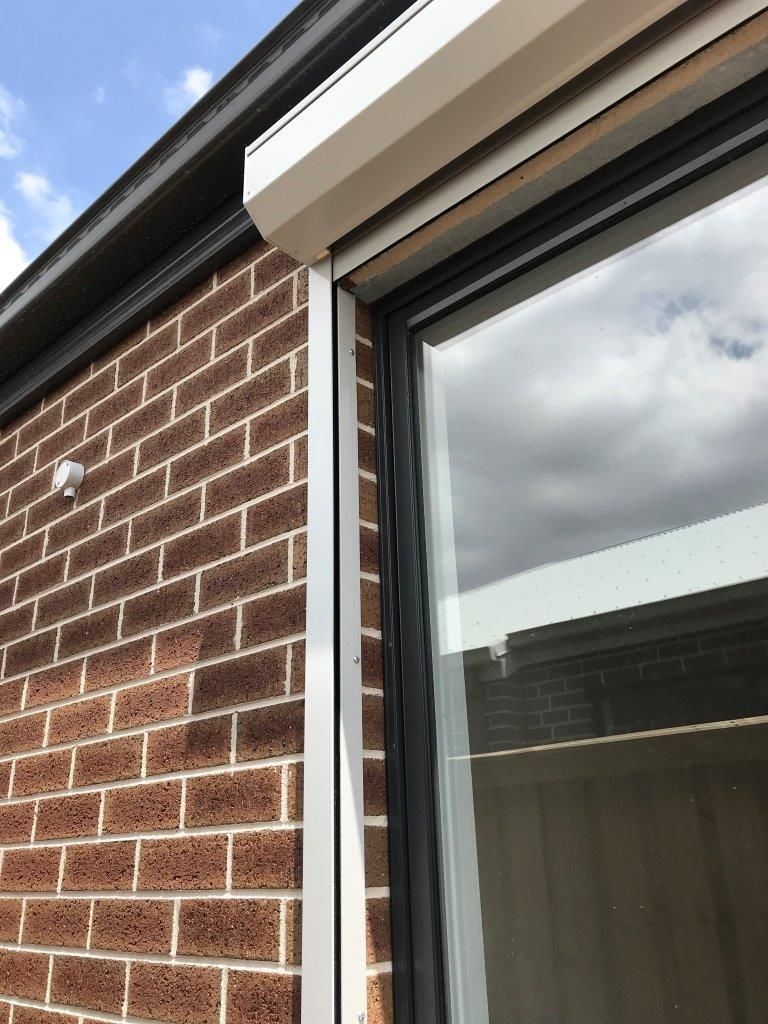 Brick exterior wall beside a window with white trim, reflecting a cloudy sky.