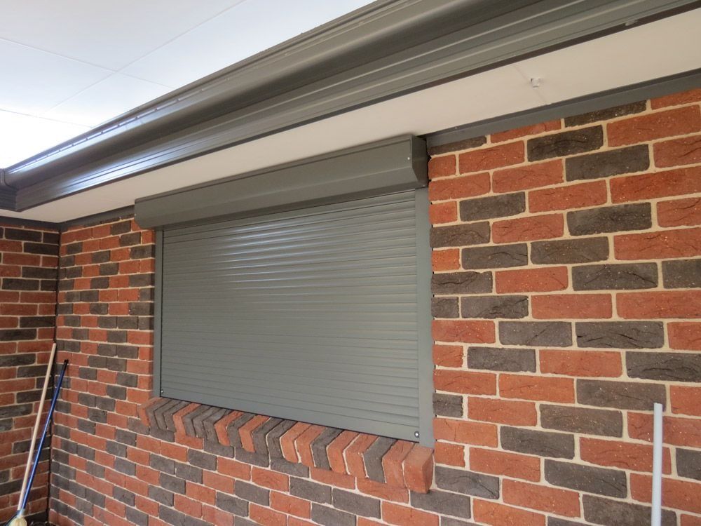 Closed gray roller shutter on a brick exterior wall under an awning
