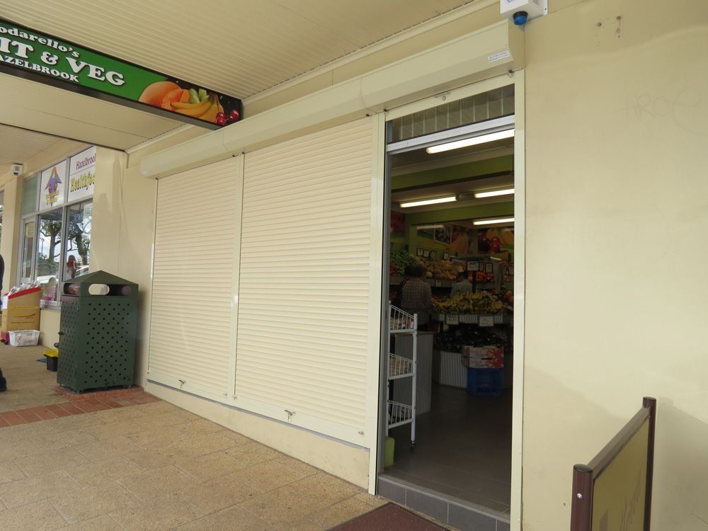 Closed storefront with white shutters beside an open shop entrance in a covered walkway