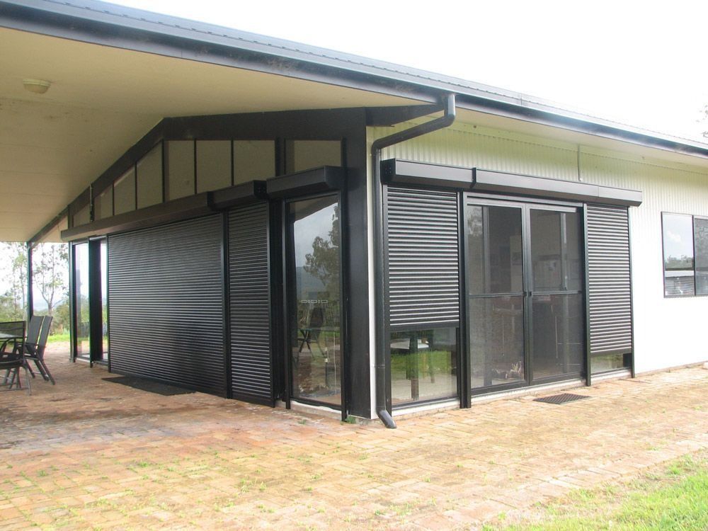 Covered patio with black roller blinds attached to a light-colored house