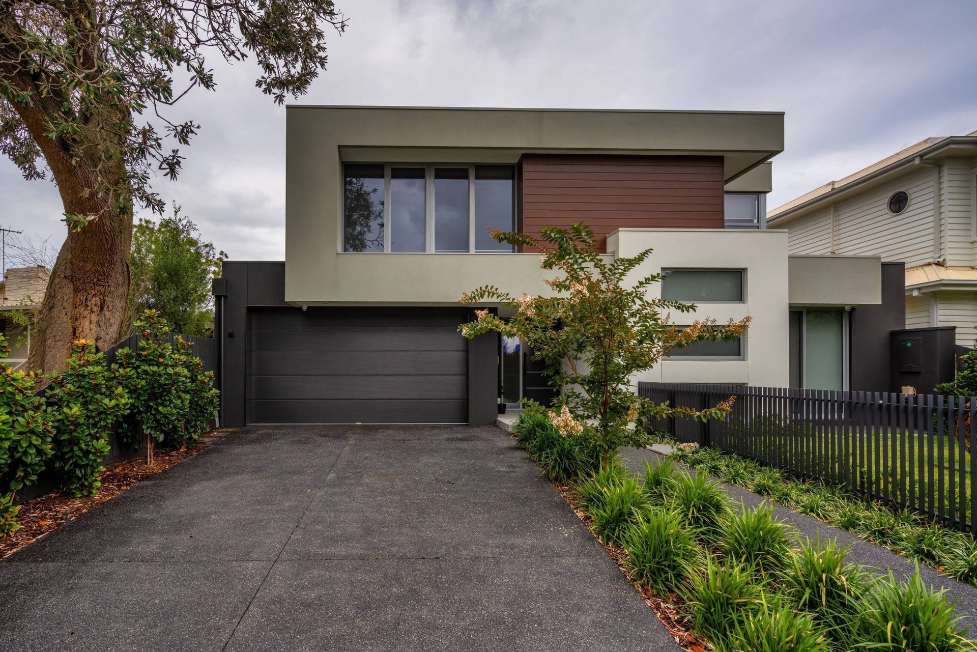 Closed metal garage door behind a green hedge and paved walkway