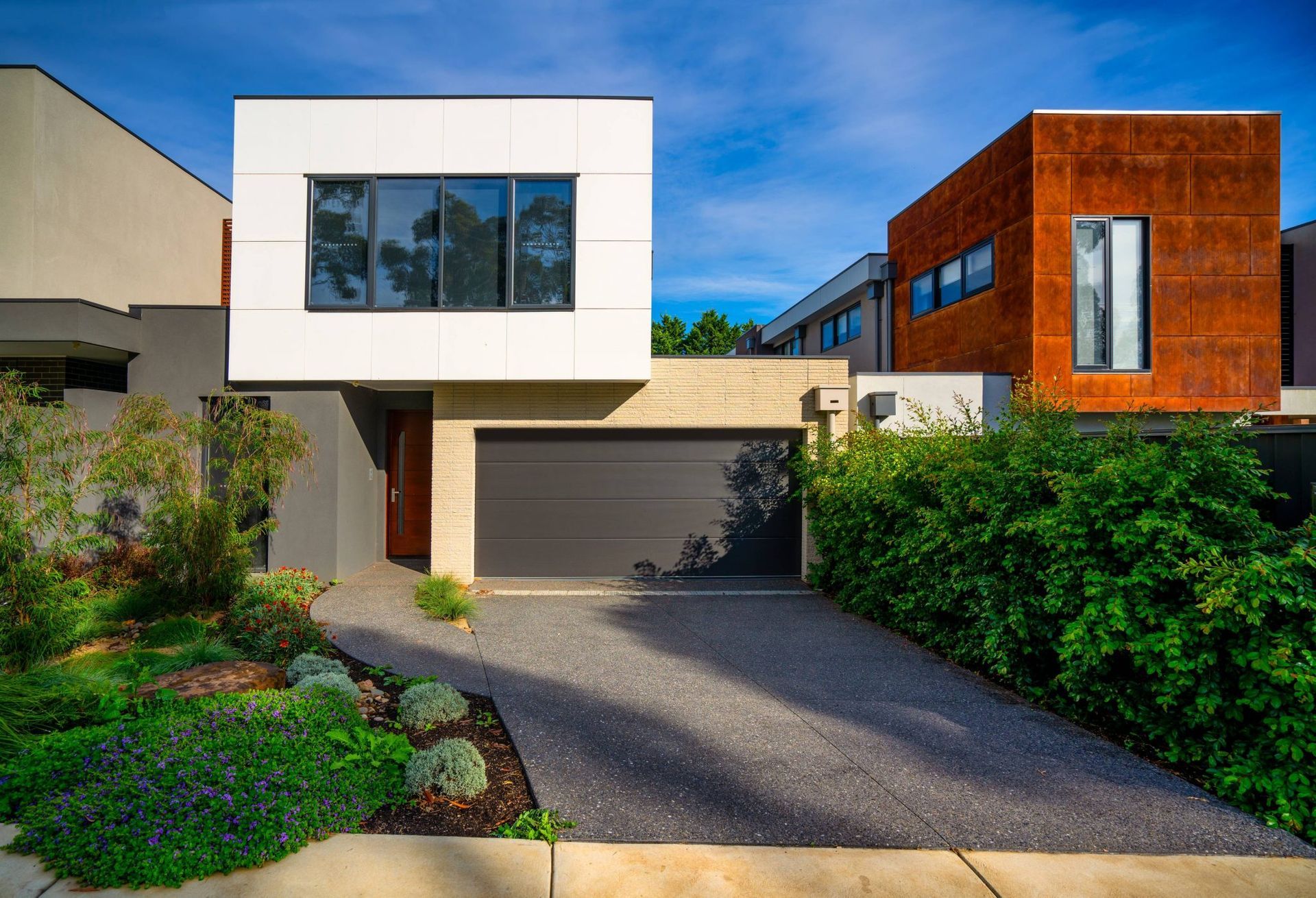 Modern two-story house with white and wood facades, garage, driveway, and landscaped front yard