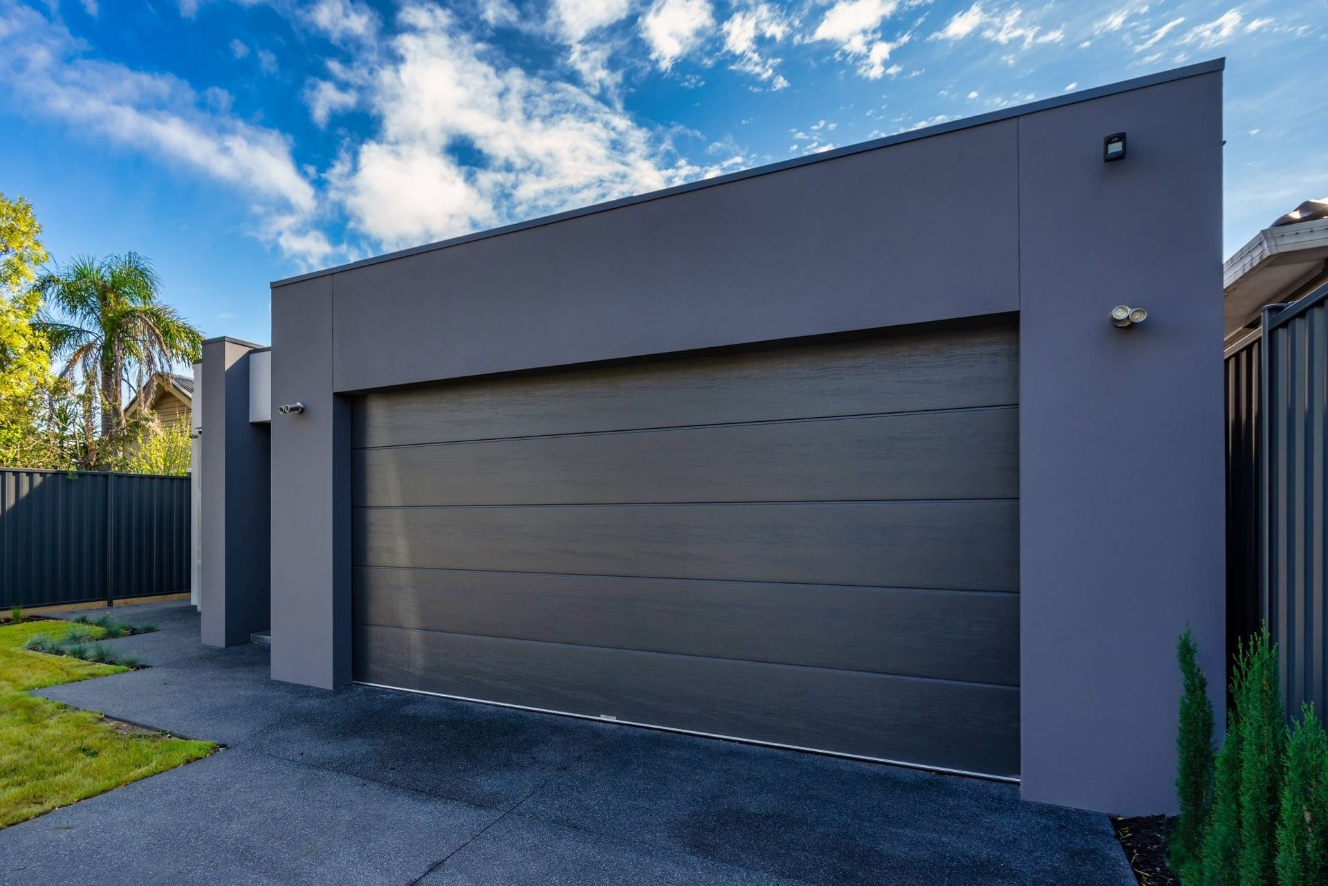 Closed metal garage door behind a green hedge and paved walkway