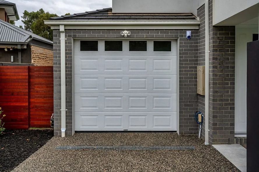 White garage door beneath a small covered entry on a brick house with gravel driveway