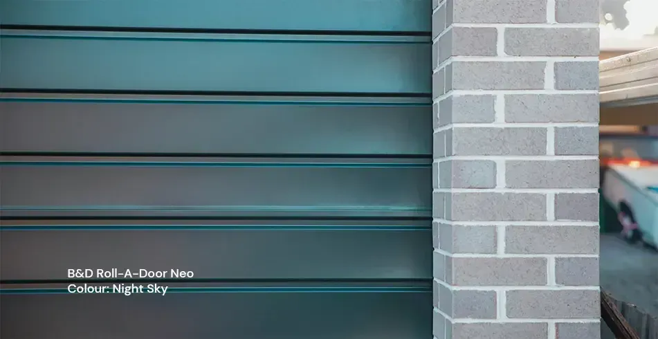 Gray garage door beside a light brick wall with a small white address sign near the bottom left.