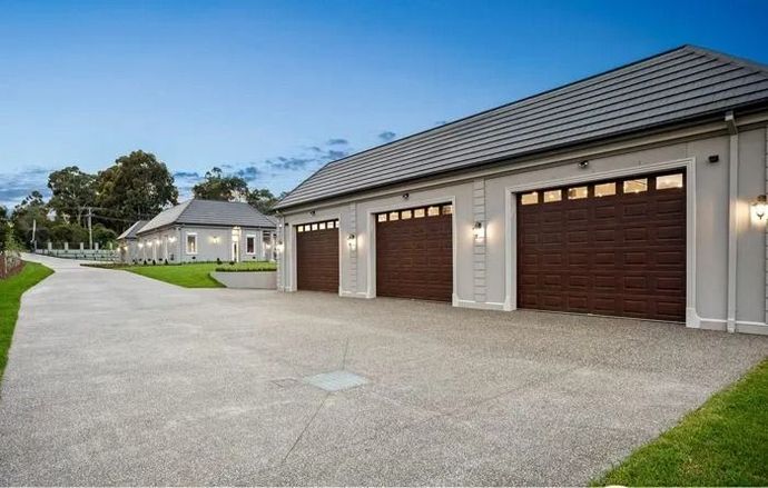 Modern single-story garage complex with brown doors and a wide gravel driveway under a blue sky