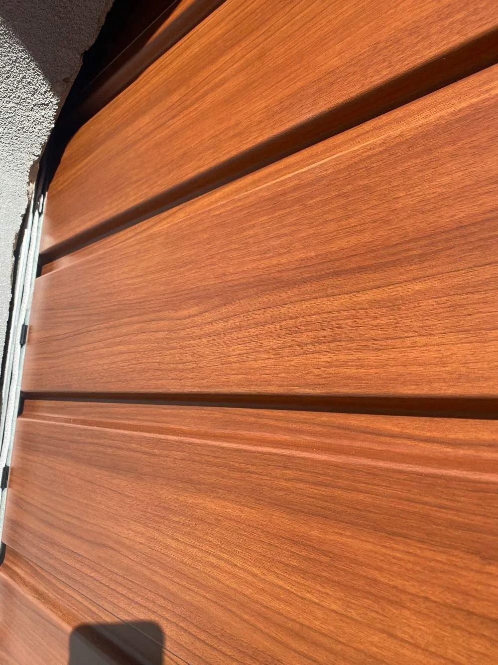 Close-up of horizontal wooden siding in warm brown tones with sunlight and shadow.