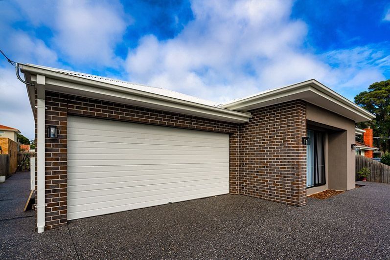 Single-story brick house with two cream garage doors and a red tile roof under a cloudy sky
