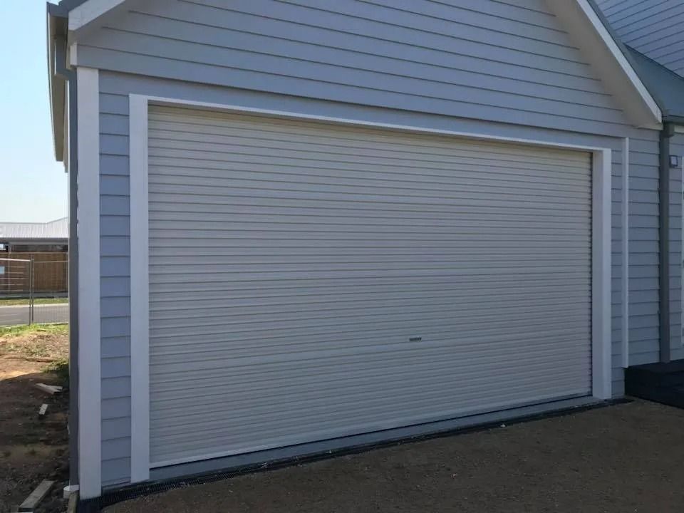 Closed white garage door on a gray-sided building with a concrete driveway.
