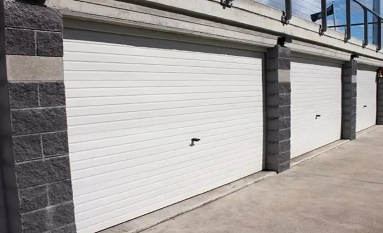 Closed metal garage door behind a green hedge and paved walkway
