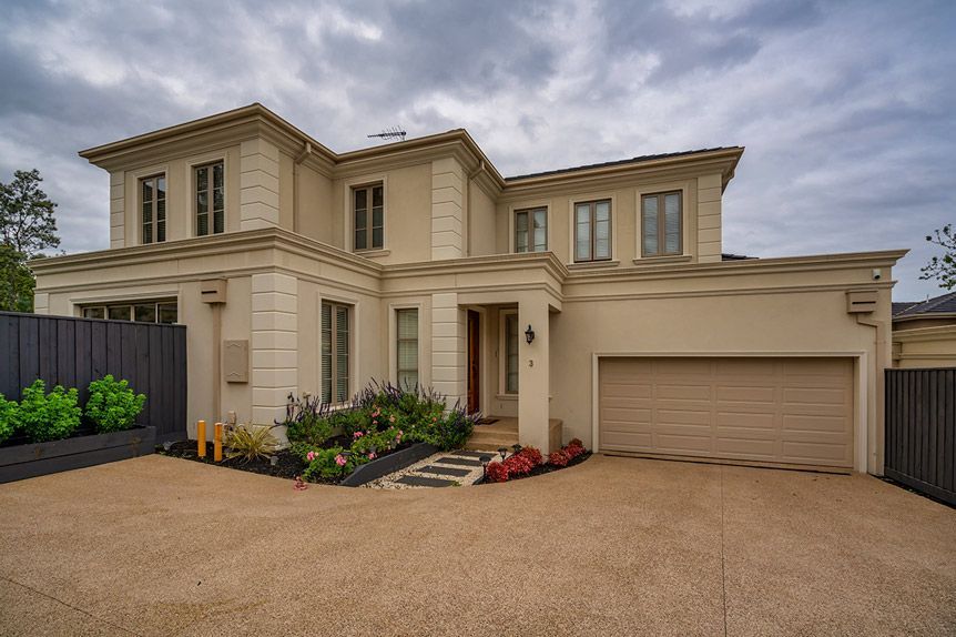 Closed metal garage door behind a green hedge and paved walkway
