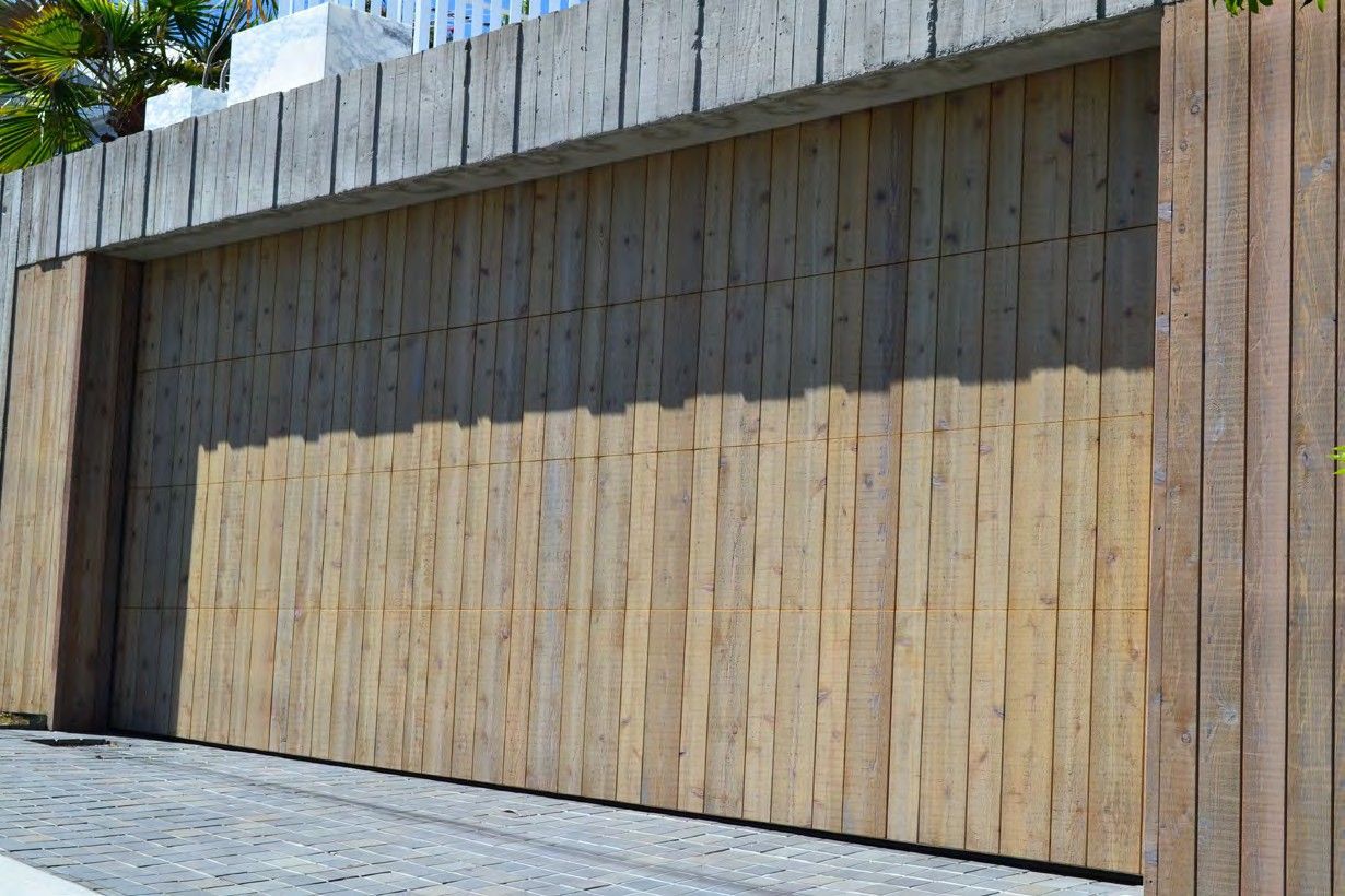 Modern wooden gate and retaining wall in bright sunlight with cobblestone pavement in front
