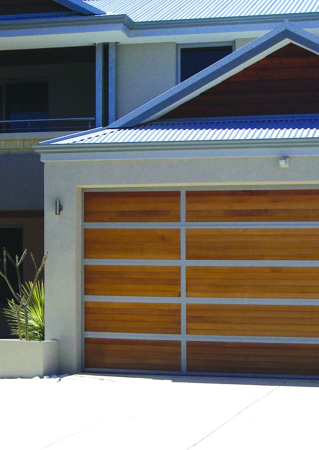 Closed metal garage door behind a green hedge and paved walkway