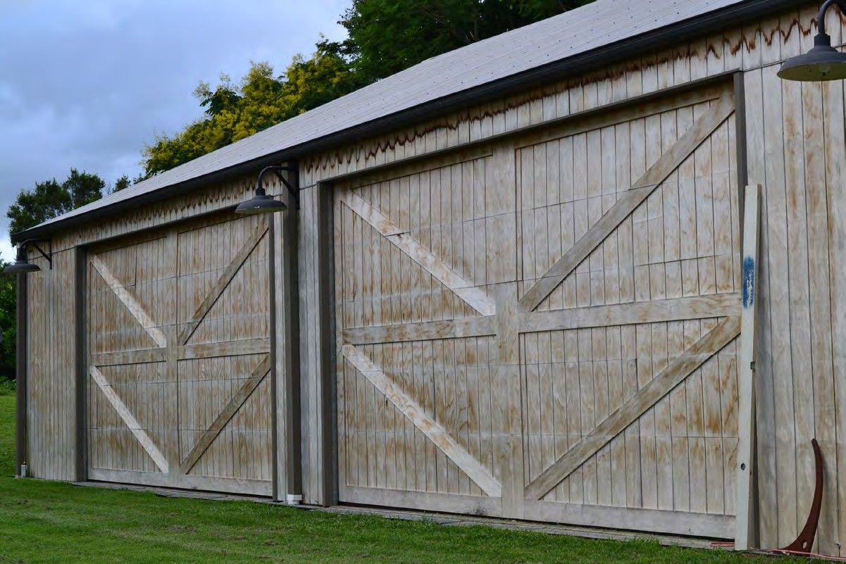 Two weathered wooden barn doors on a white shed with a sloped metal roof and grassy foreground.