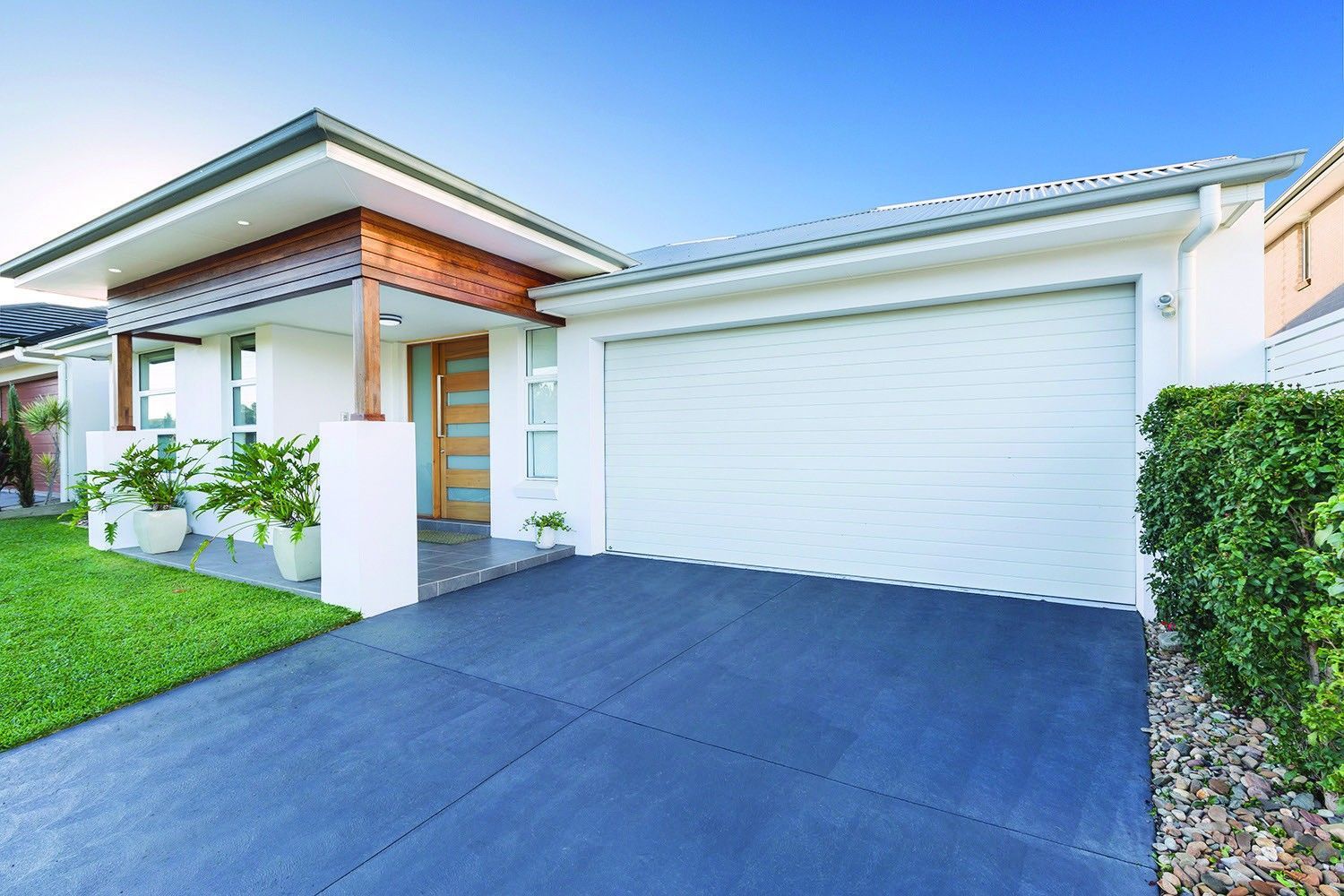 Modern single-story house exterior with white garage, blue driveway, and manicured lawn