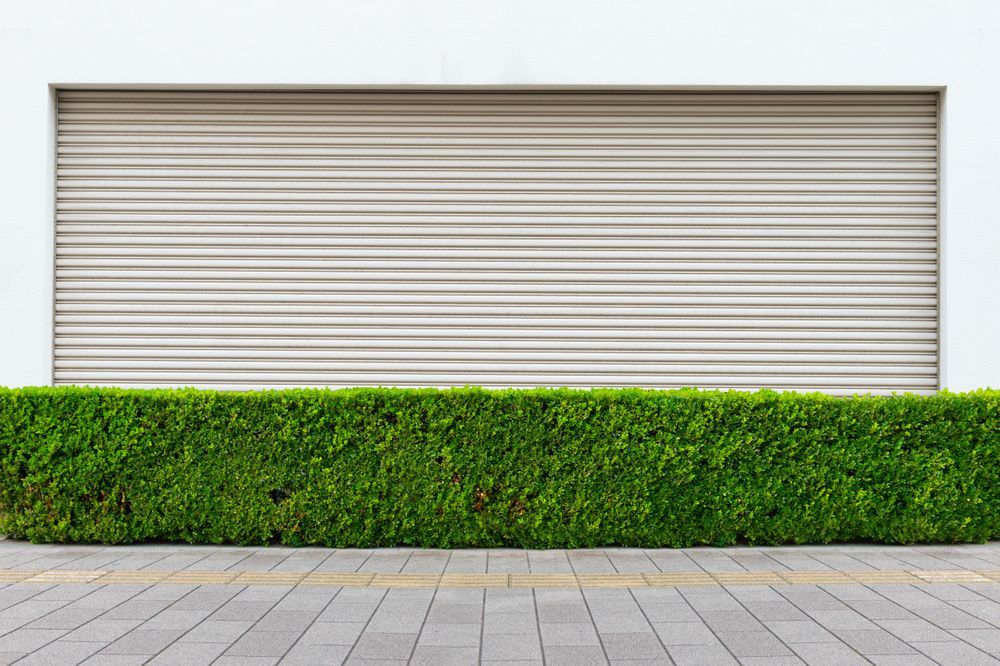 Closed metal garage door behind a green hedge and paved walkway