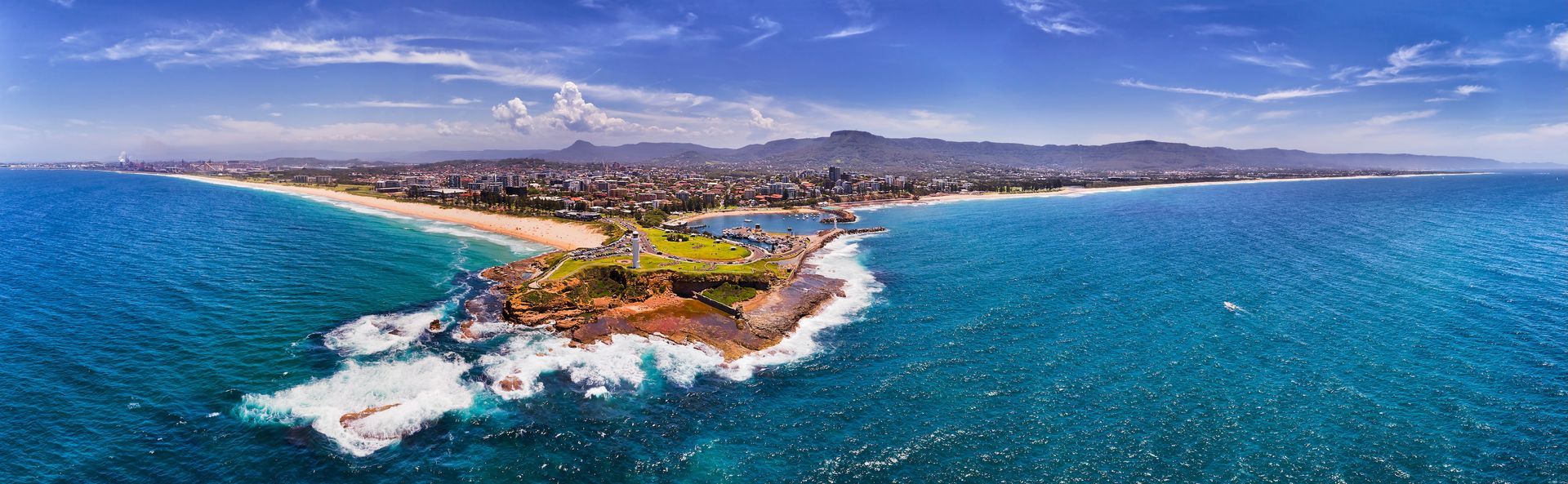 Aerial view of a turquoise tropical coastline with waves, a sandy beach, and mountains in the distance