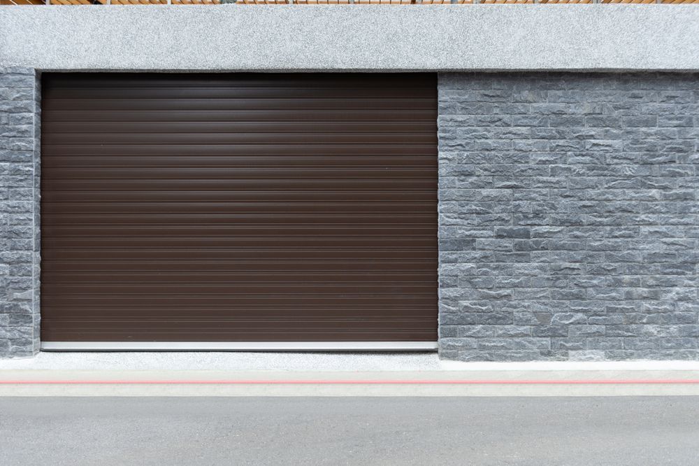 Closed brown storefront shutter on a gray stone wall above a red curb line