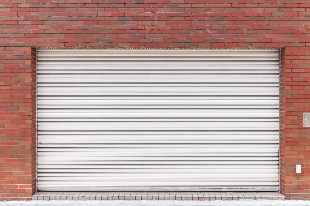 Closed white roll-up garage door set in a red brick wall