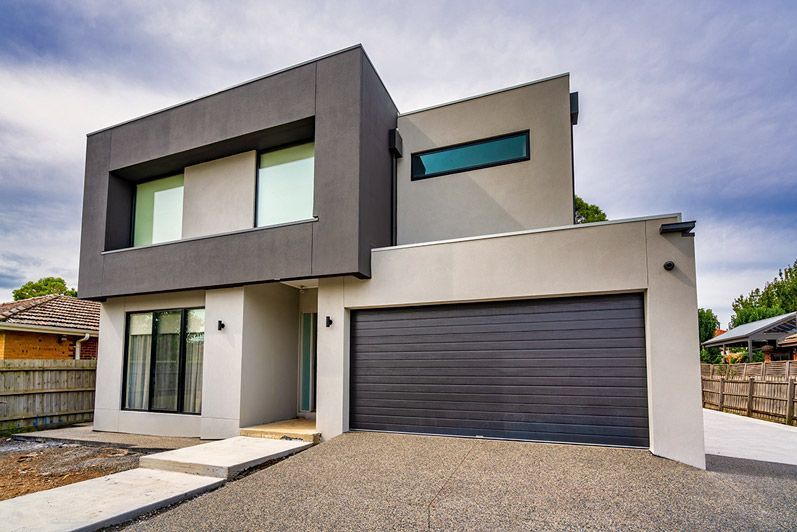 Closed metal garage door behind a green hedge and paved walkway