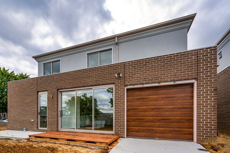 Modern two-story brick house with large windows, wooden garage door, and small front deck