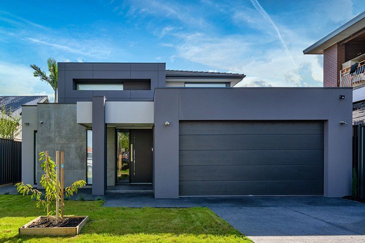 Closed metal garage door behind a green hedge and paved walkway