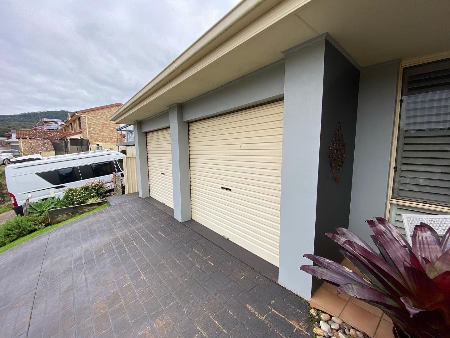 Driveway beside a row of cream garage doors and gray columns, with a white van parked below.