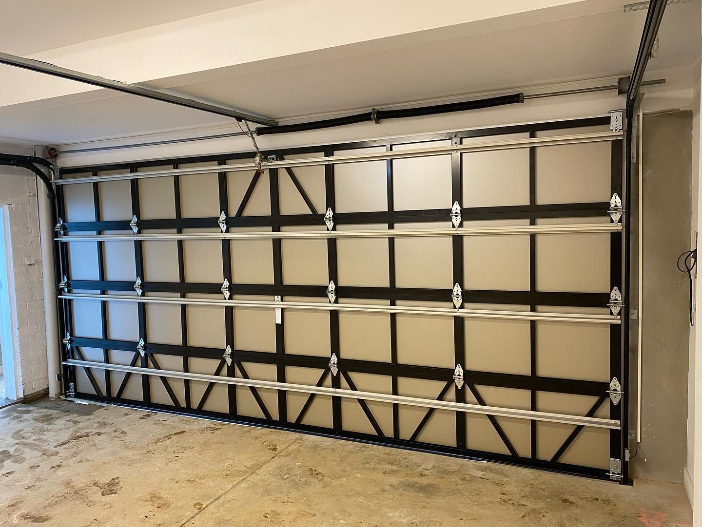 Interior view of a garage with a black sectional garage door and beige walls and floor.