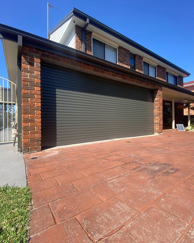 Brick house exterior with a closed gray garage door and red driveway under a blue sky