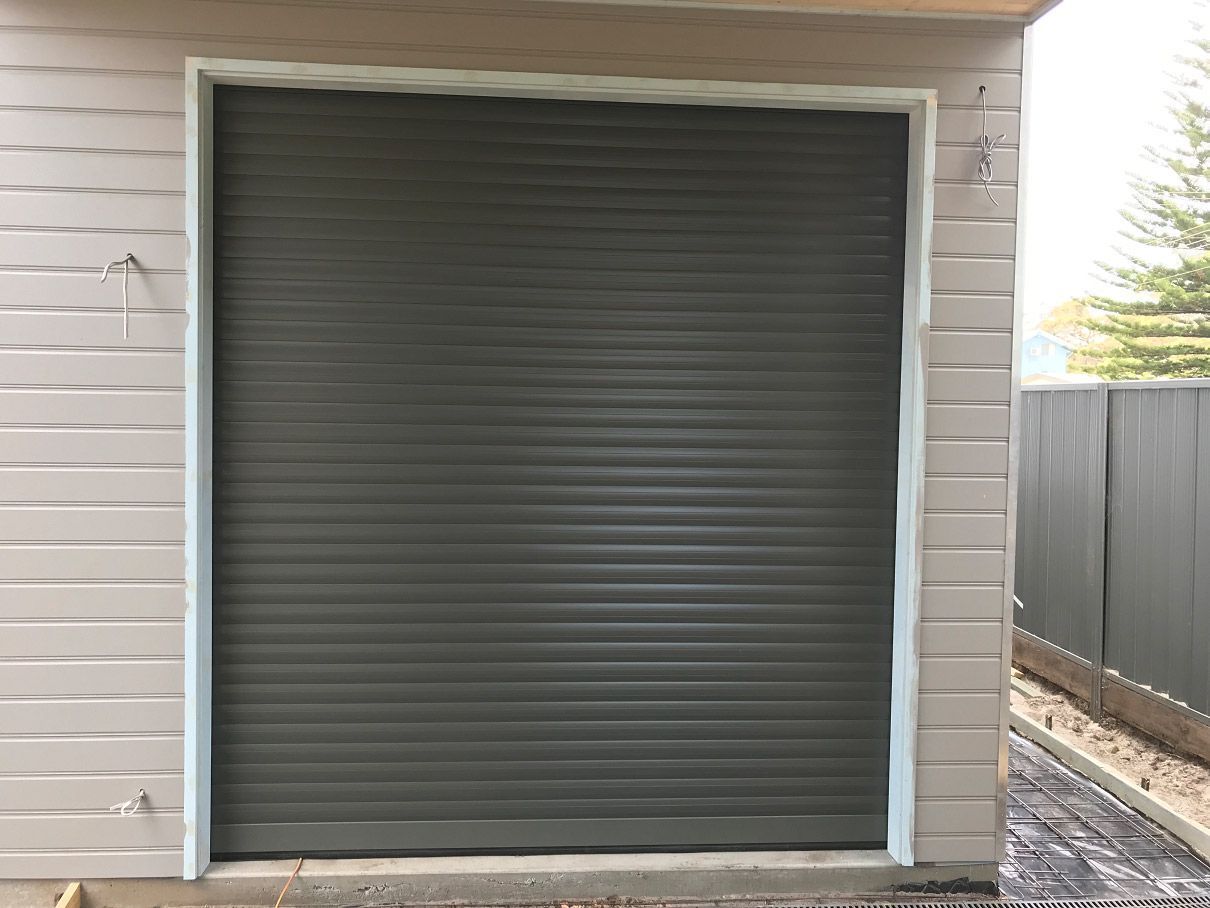 Closed gray roll-up garage door on a white-sided exterior wall.