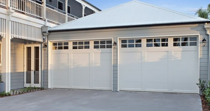 Two white garage doors on a beige house exterior with a paved driveway