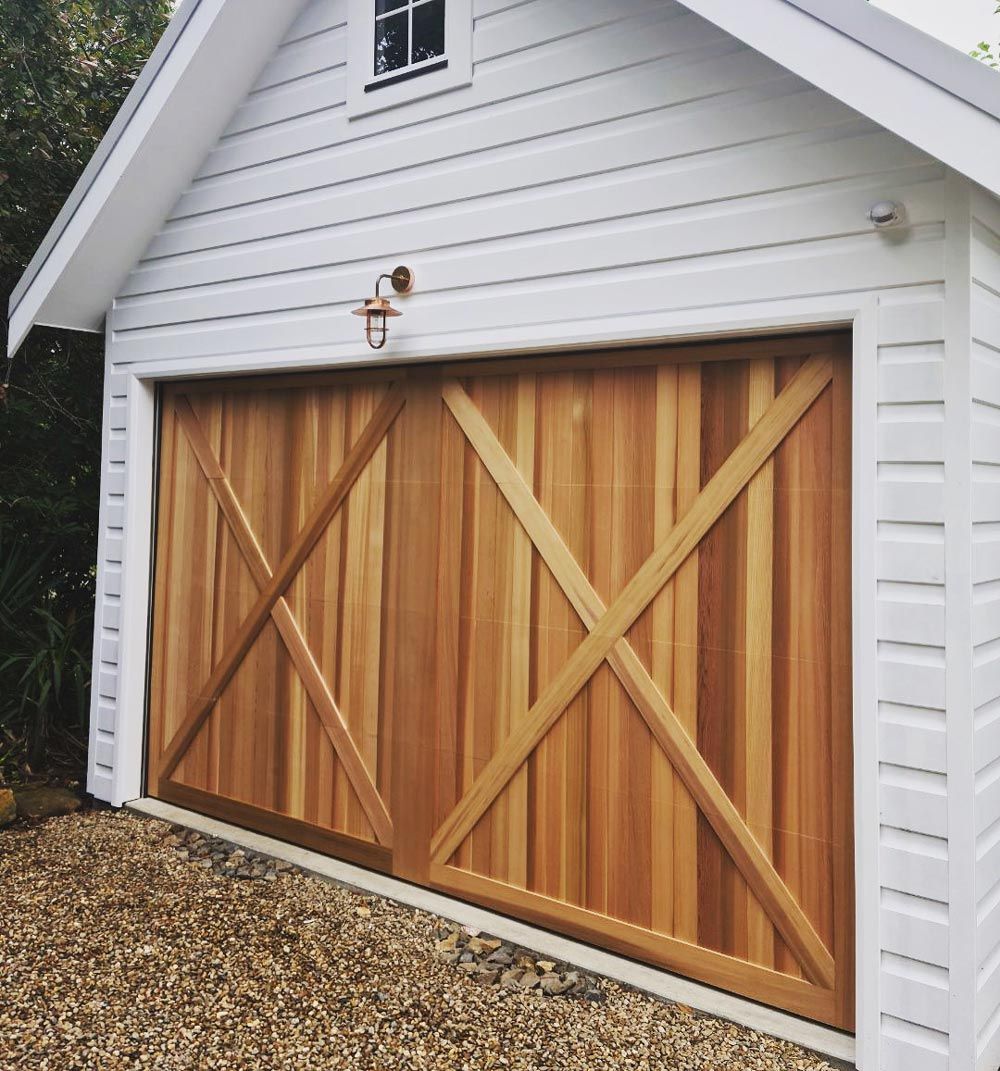 Wooden double garage door with X-braced panels on a white-sided house