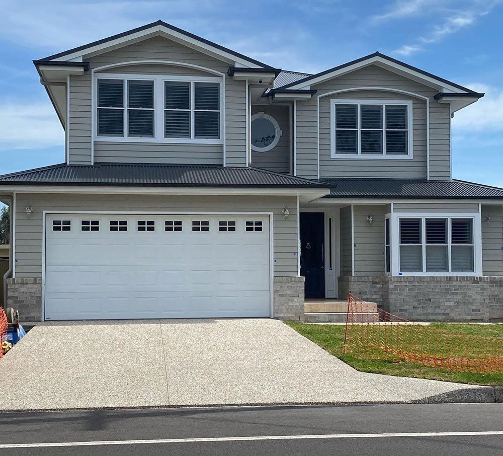 Two-story suburban house with white garage door, gray siding, and a concrete driveway under a blue sky