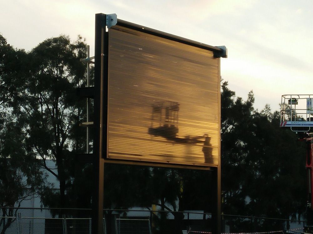 Large outdoor screen with a golden sunset reflection, silhouetted by trees in the background