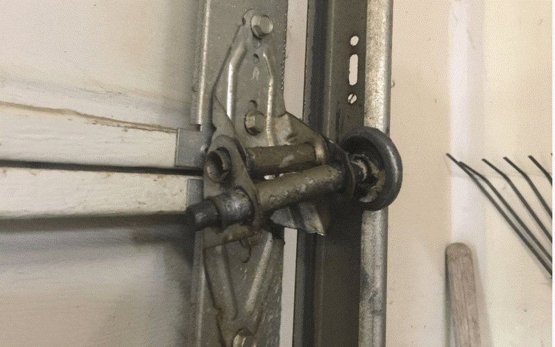 Close-up of a metal garage door latch and roller mechanism on a light-colored wall