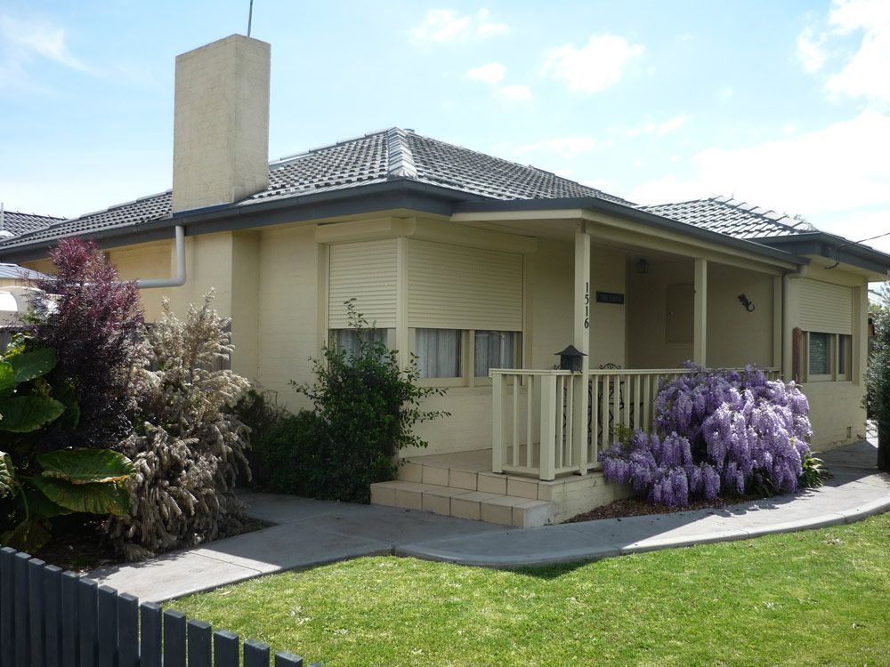 Single-story beige house with a front porch, tiled roof, and green lawn