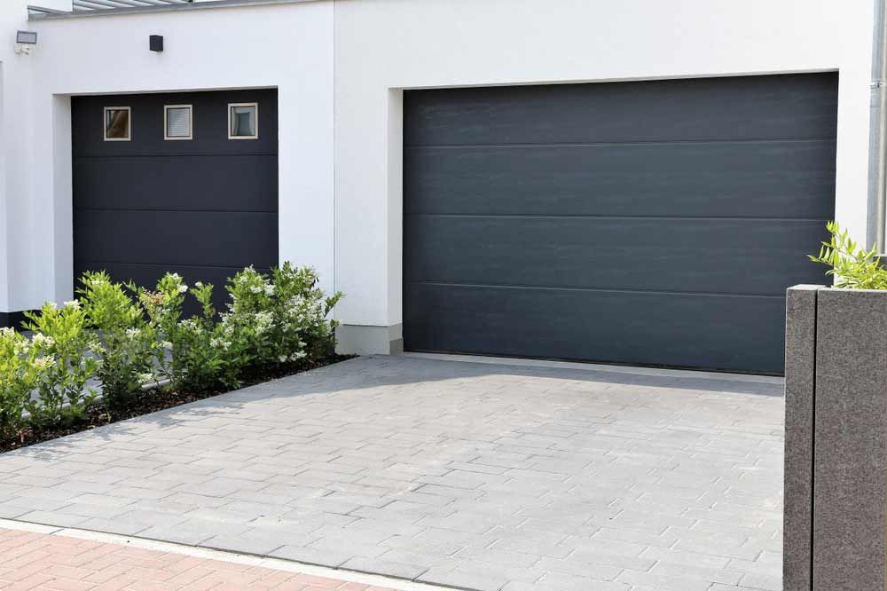 Modern house exterior with a gray garage door, small side door, and driveway lined with shrubs