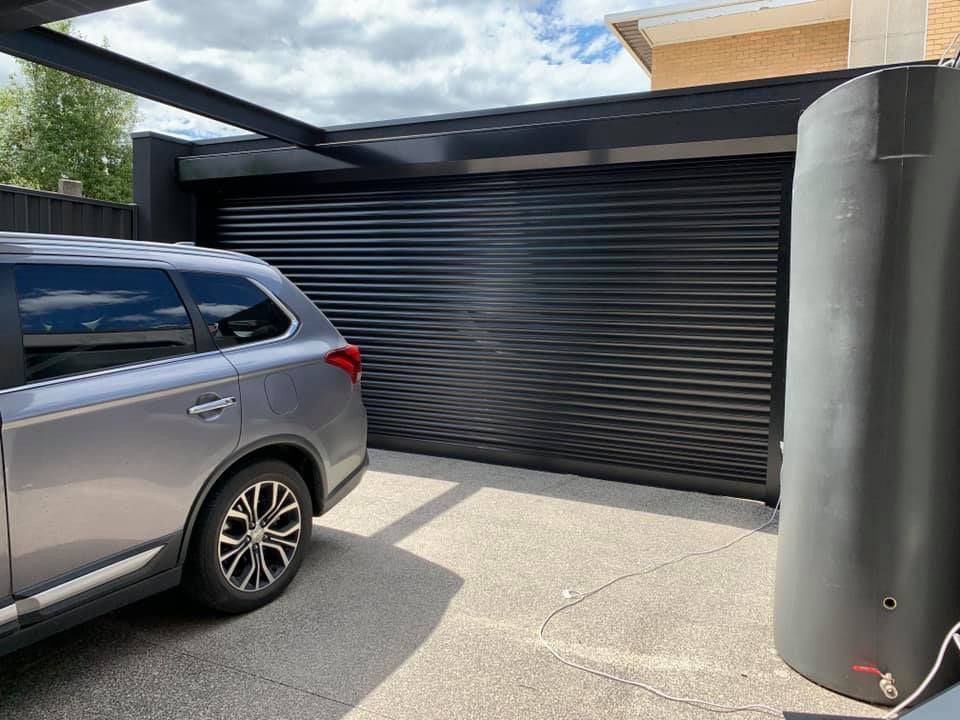 Gray SUV parked in front of a black rolling garage door under a covered driveway