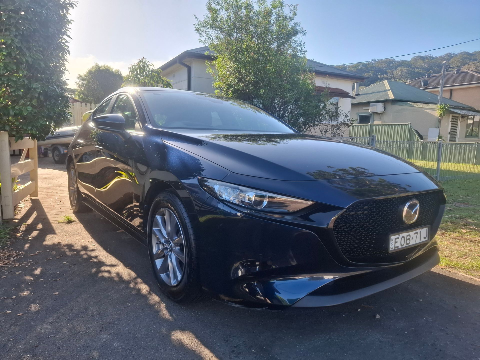 A black mazda 3 is parked in a driveway in front of a house. — Ocean Glow Car Detailing in Long Jetty NSW