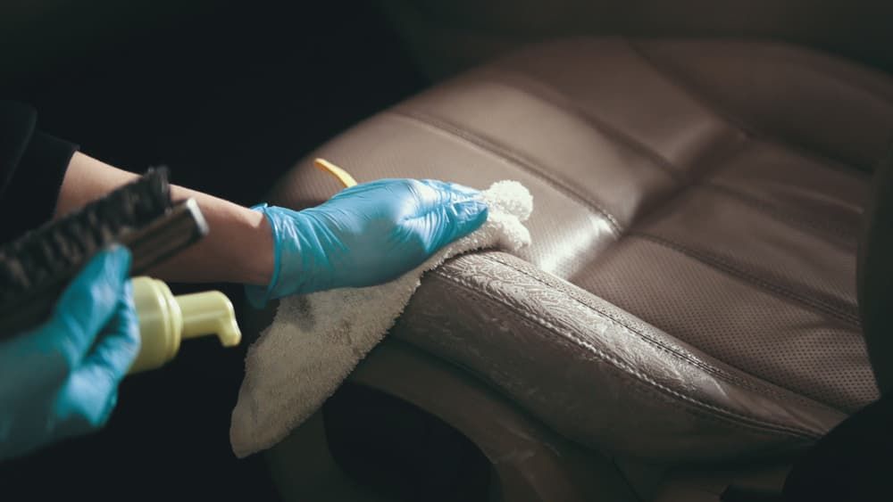 A Person Wearing Blue Gloves Is Cleaning a Leather Seat in A Car — Ocean Glow Mobile Detailing In Lake Macquarie, NSW