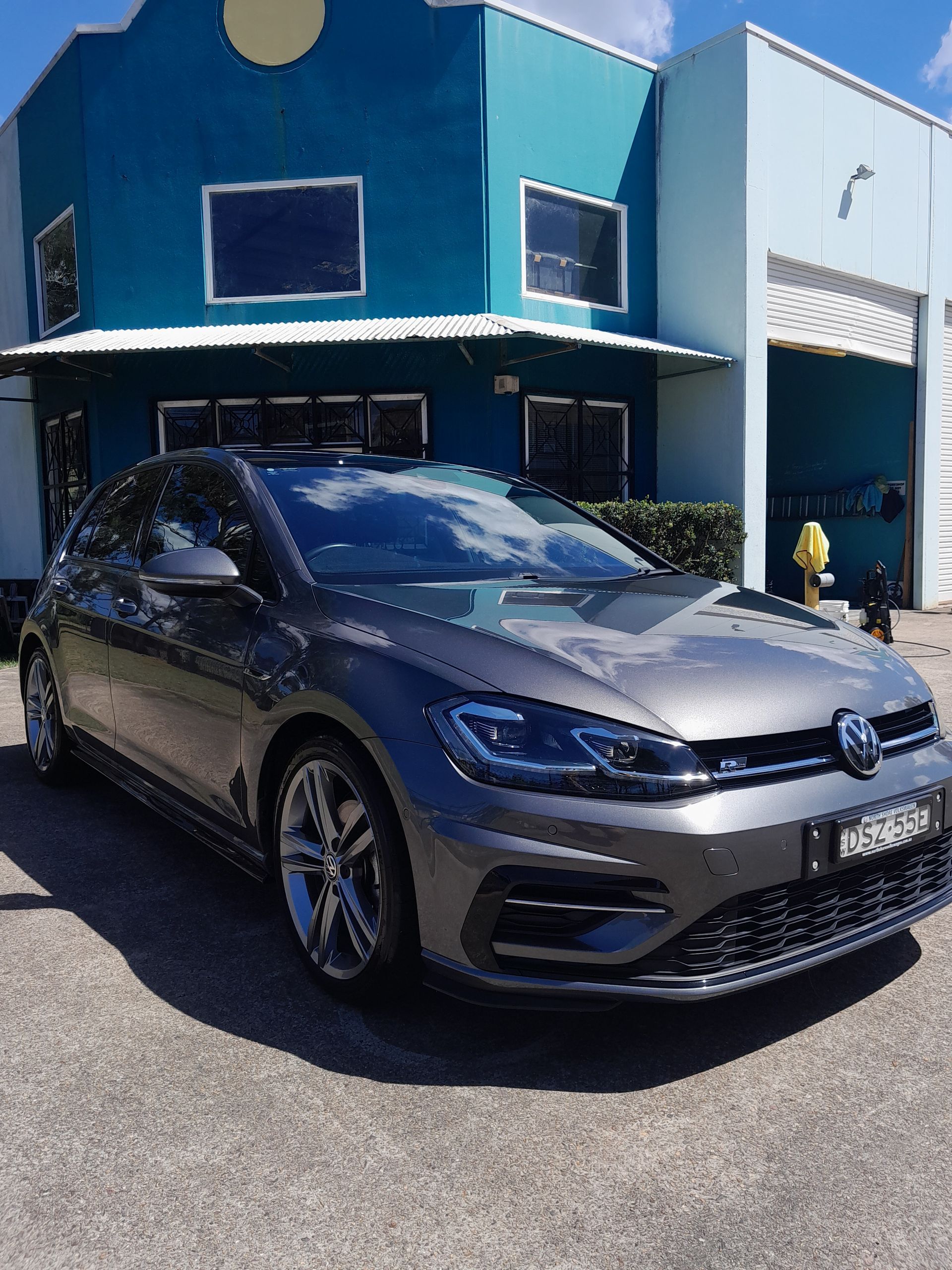 A volkswagen golf r is parked in front of a blue building. — Ocean Glow Car Detailing in Long Jetty NSW