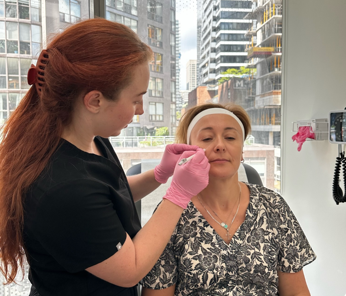 A woman wearing pink gloves is applying makeup to another woman 's face.