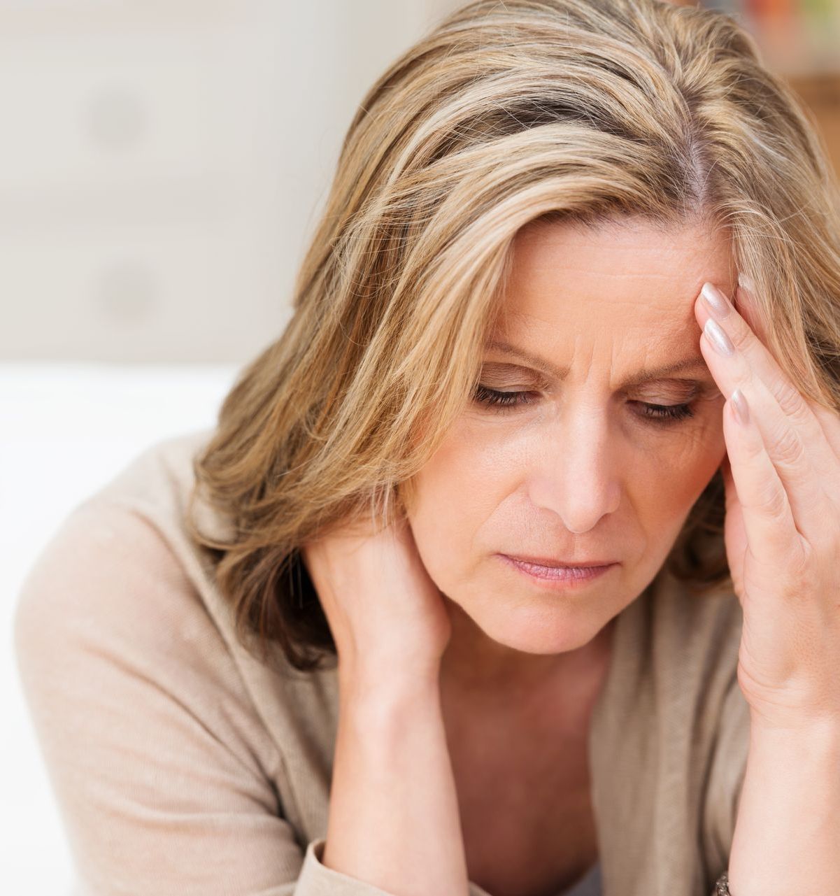 A woman is sitting on a couch holding her head.