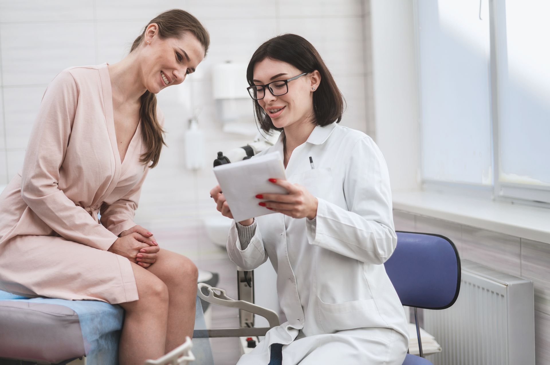 A female doctor is talking to a female patient while looking at a tablet.